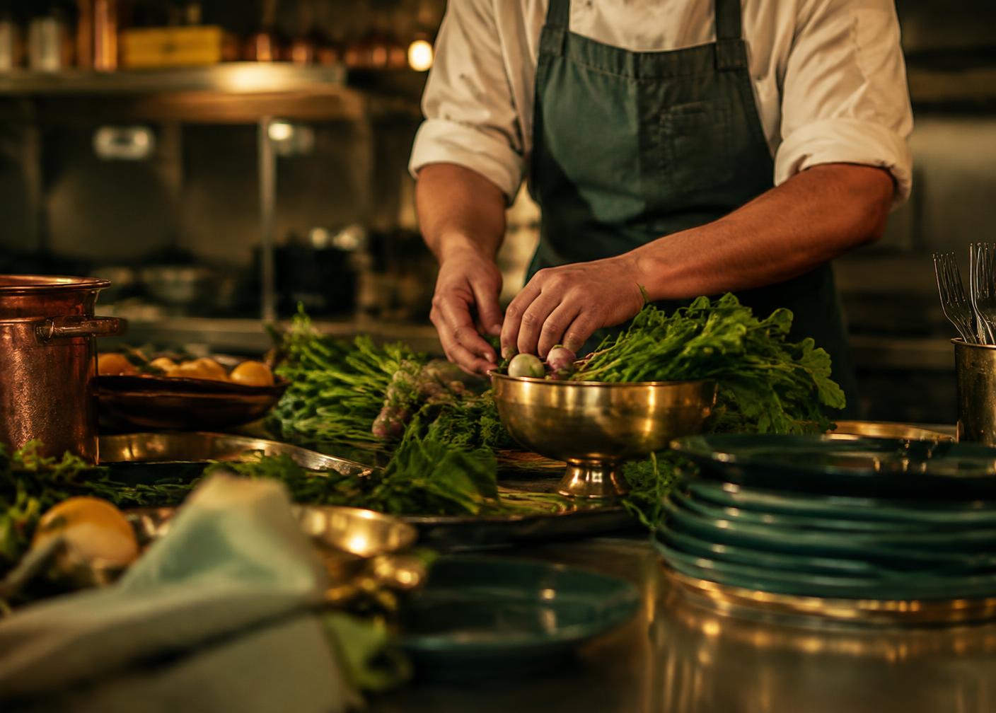 A chef preparing fresh seasonal greens in a warmly lit kitchen